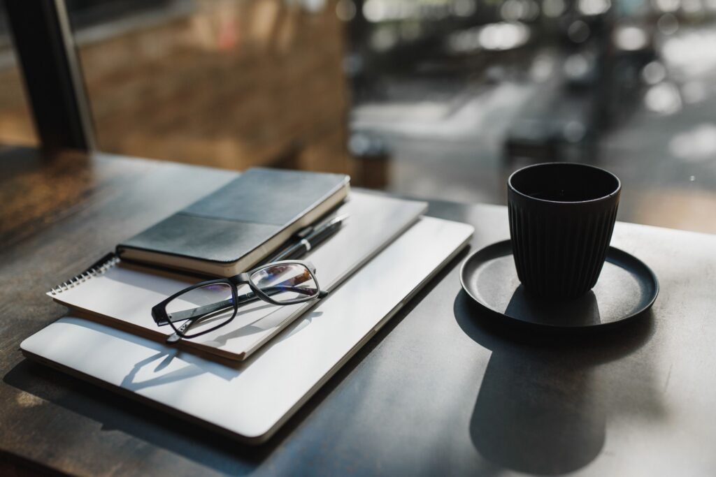 A calm morning workspace with sunlight, a notebook, coffee, and a simple priority list,
