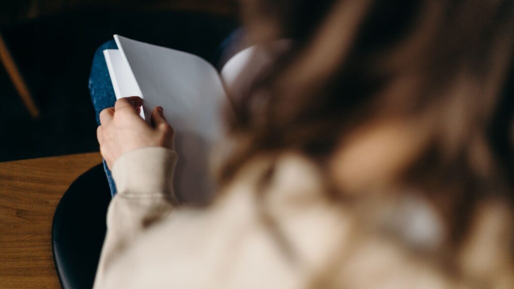 A person sitting quietly with a journal near a window, reflecting with calmness and self-awareness
