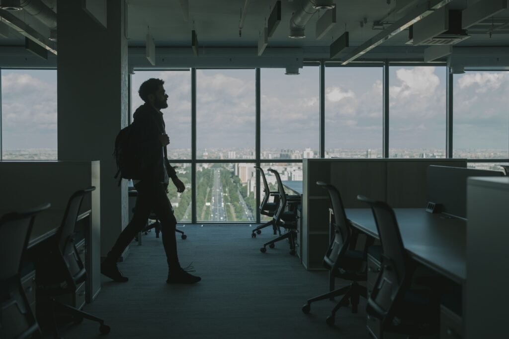 A professional standing confidently near a window or walking through a modern workplace