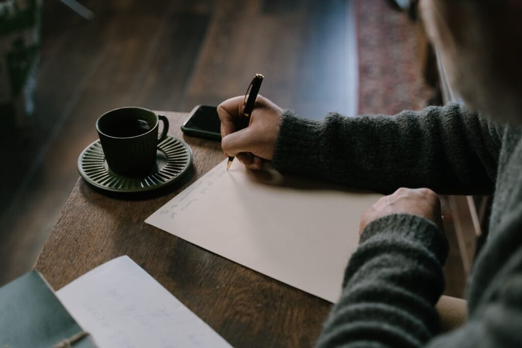 A person writing a letter in a notebook beside a window