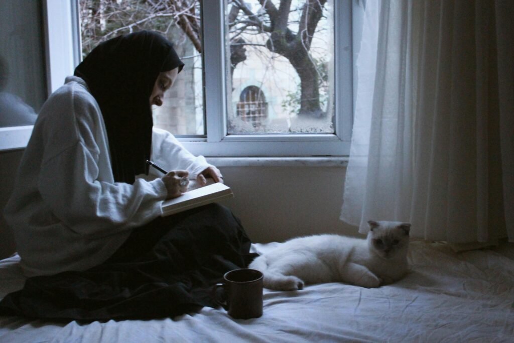 A peaceful person sitting near a window with soft natural light, a notebook, tea, and a quiet city background