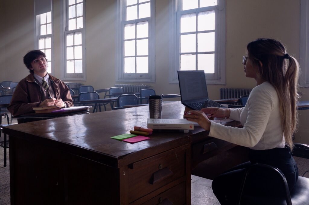 A professional conversation between two people at a desk with notebooks and a laptop