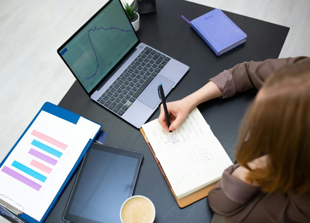 A person writing in a notebook beside a laptop with a clean document open