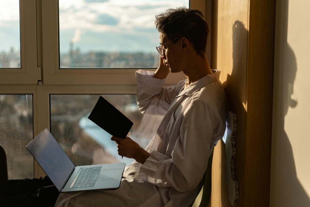 A calm person sitting by a window with a notebook, reflecting peacefully