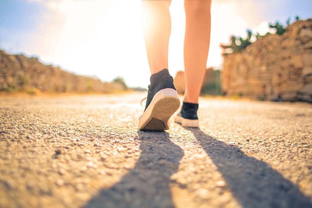 A person walking slowly on a long road toward sunrise