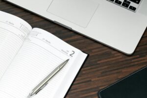 A clean desk with a notebook, calendar, laptop, and pen