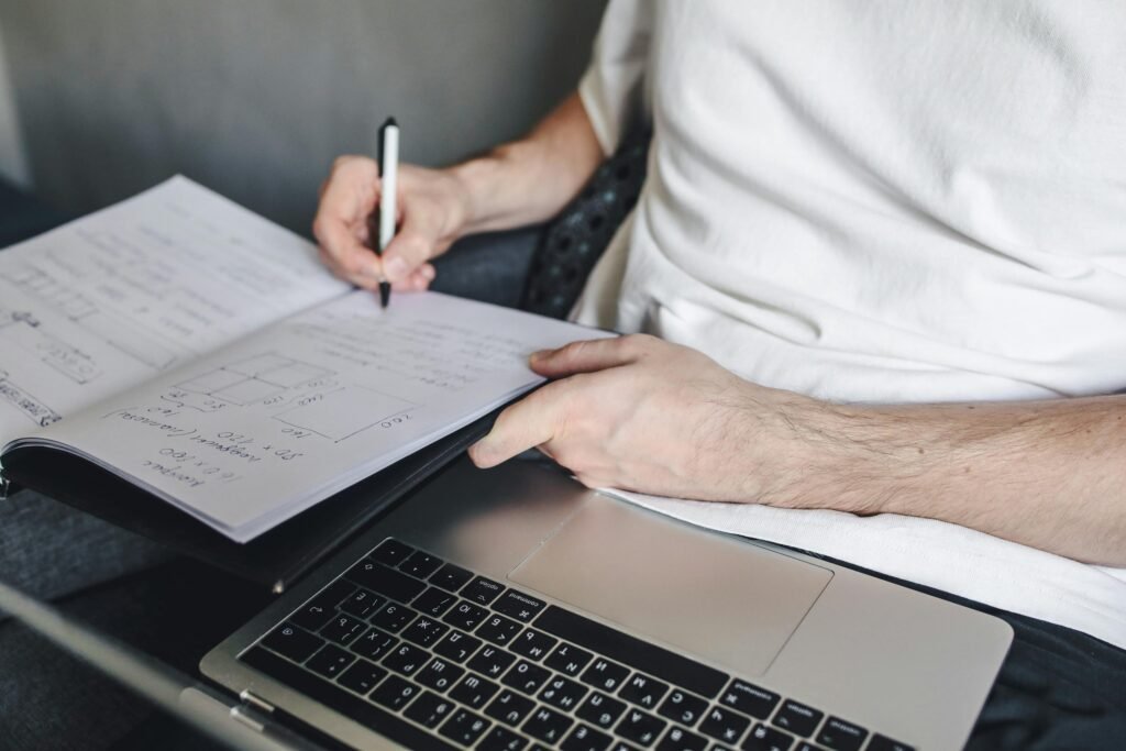 A person studying at a desk with a notebook, laptop, flashcards, and a simple skill-learning plan