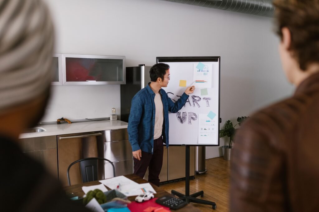 A confident professional presenting ideas in front of a small audience or meeting room, with a simple slide deck or whiteboard showing clear points and organized visuals.