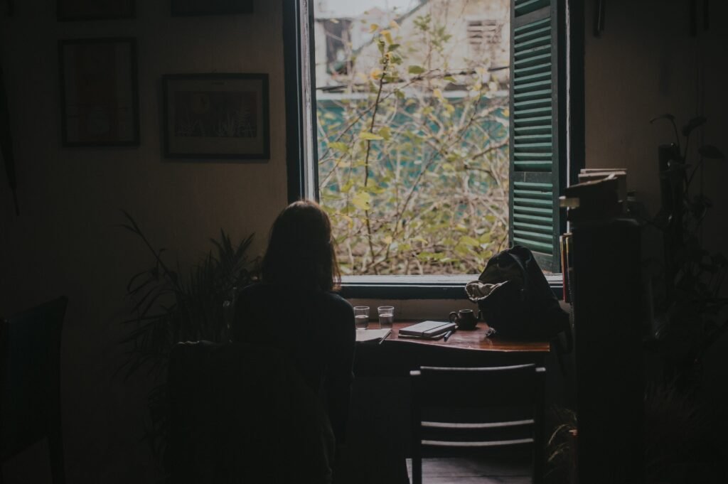 A person sitting quietly with a journal near a window, reflecting on personal needs, emotions, boundaries, and life direction in a calm and peaceful setting.