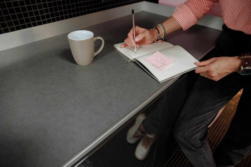 A person writing daily priorities in a notebook beside a cup of coffee and a clean workspace