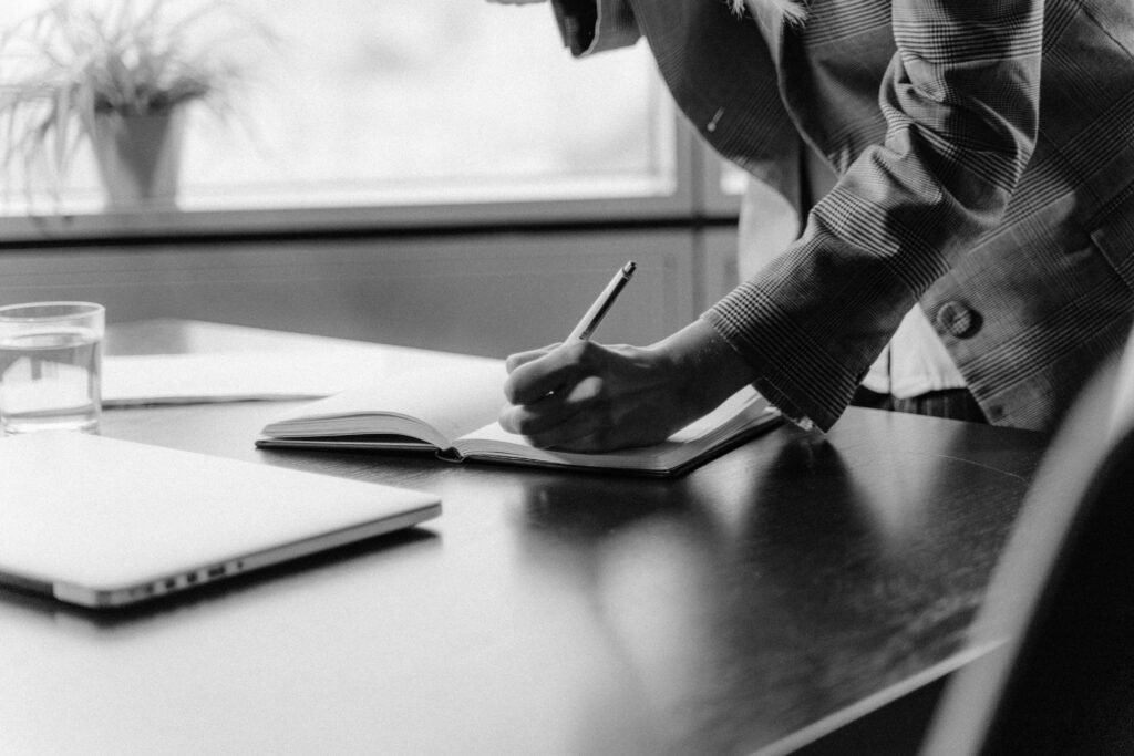 A person restarting work at a clean desk with a notebook, laptop, and simple priority lis