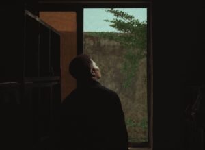 A person standing quietly near a window or open road, looking thoughtful but calm