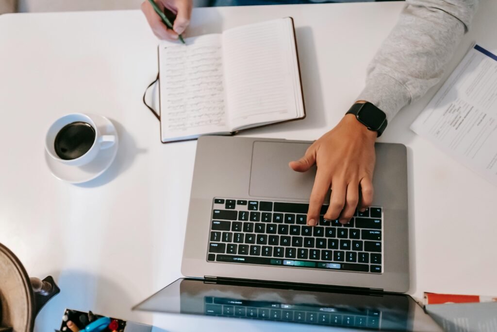 A clean notebook showing three daily priorities beside a laptop, pen, and cup of coffee